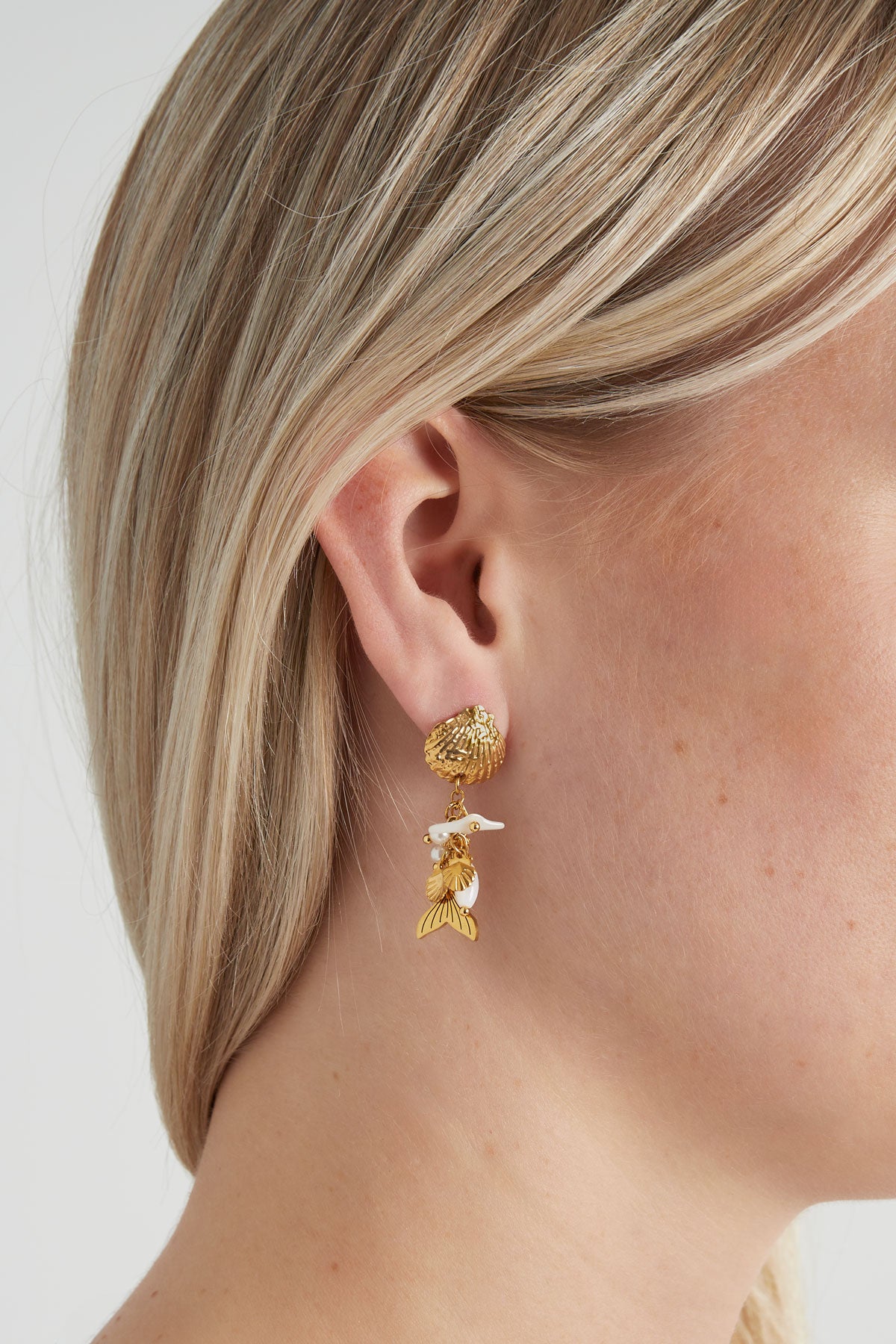 Die goldfarbenen Ohrringe "Dreamy Waterworld" aus Edelstahl im Muscheldesign, verziert mit Steinchen, Perlen und Meerjungfrauen-Flosse