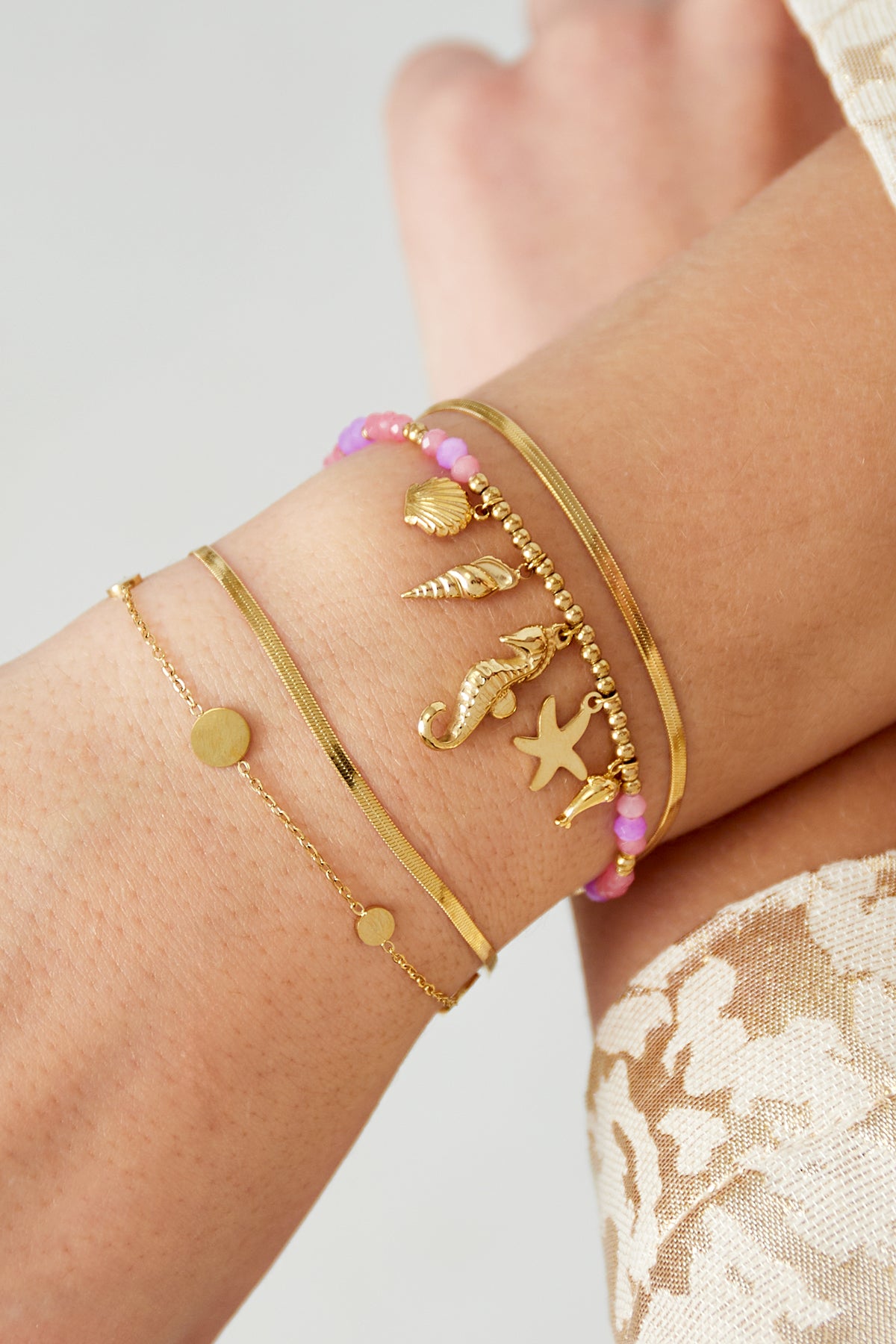 Buntes Perlenarmband mit goldenen Anhängern, darunter Muscheln, Seepferdchen und Delfin, ideal für den Sommerlook.