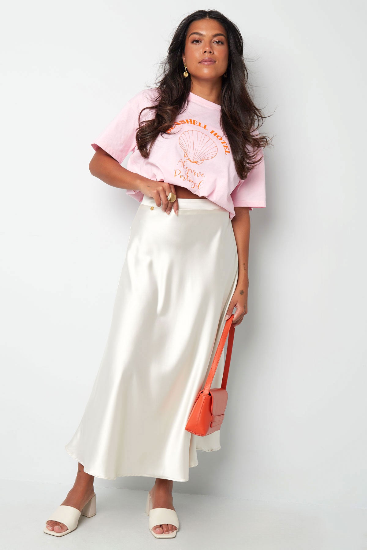 Seashell Hotel Shirt Rosa – lockeres T-Shirt in zartem Rosa mit maritimem Muschel-Design und leuchtender orangefarbener Schrift.