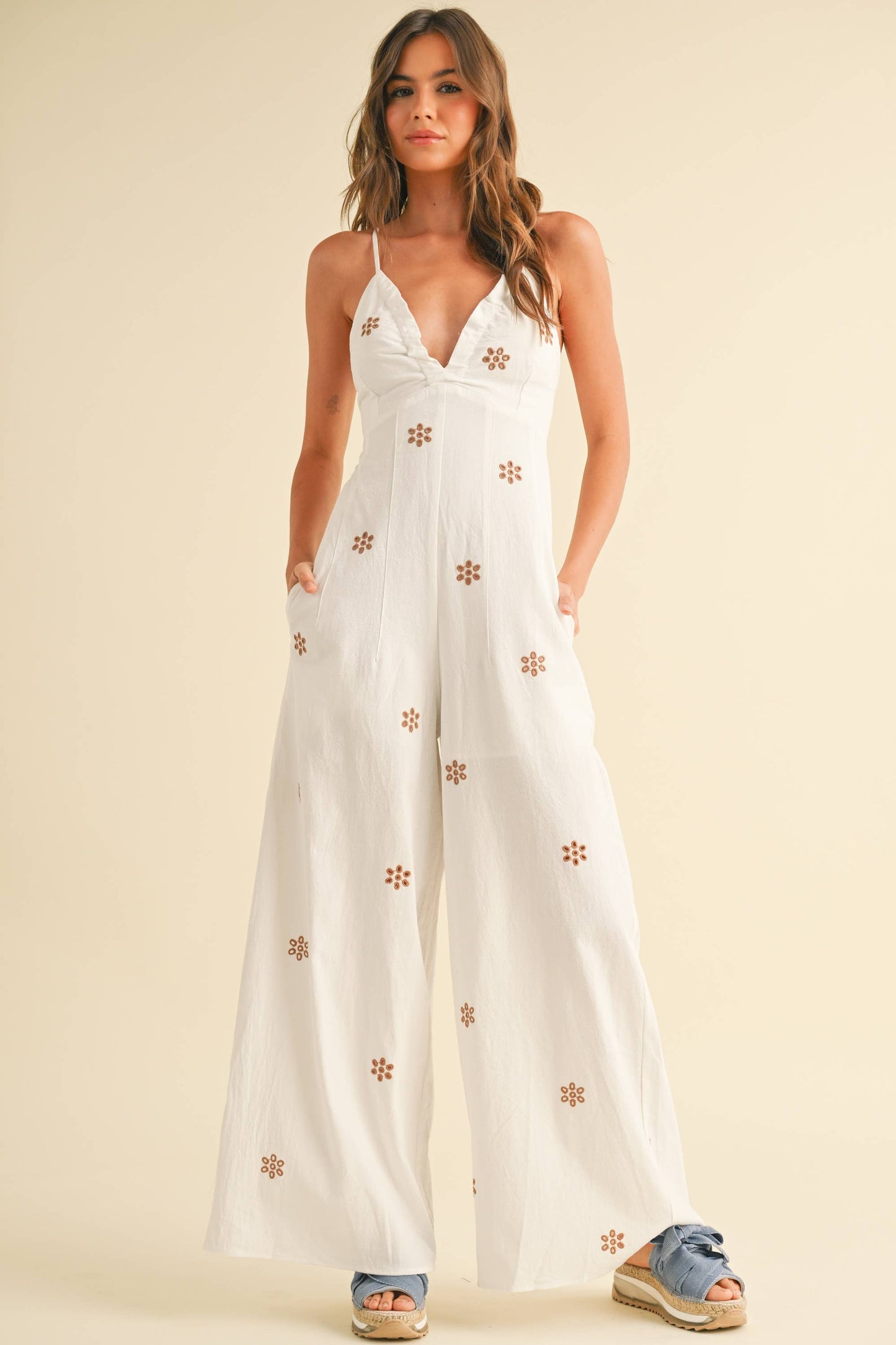 Sommerlicher Jumpsuit mit Stickereien und Schleifen – Der Jumpsuit mit gekreuzten Trägern, tiefem Dekolleté und floralen Stickereien ist der perfekte Begleiter für warme Frühlingstage.